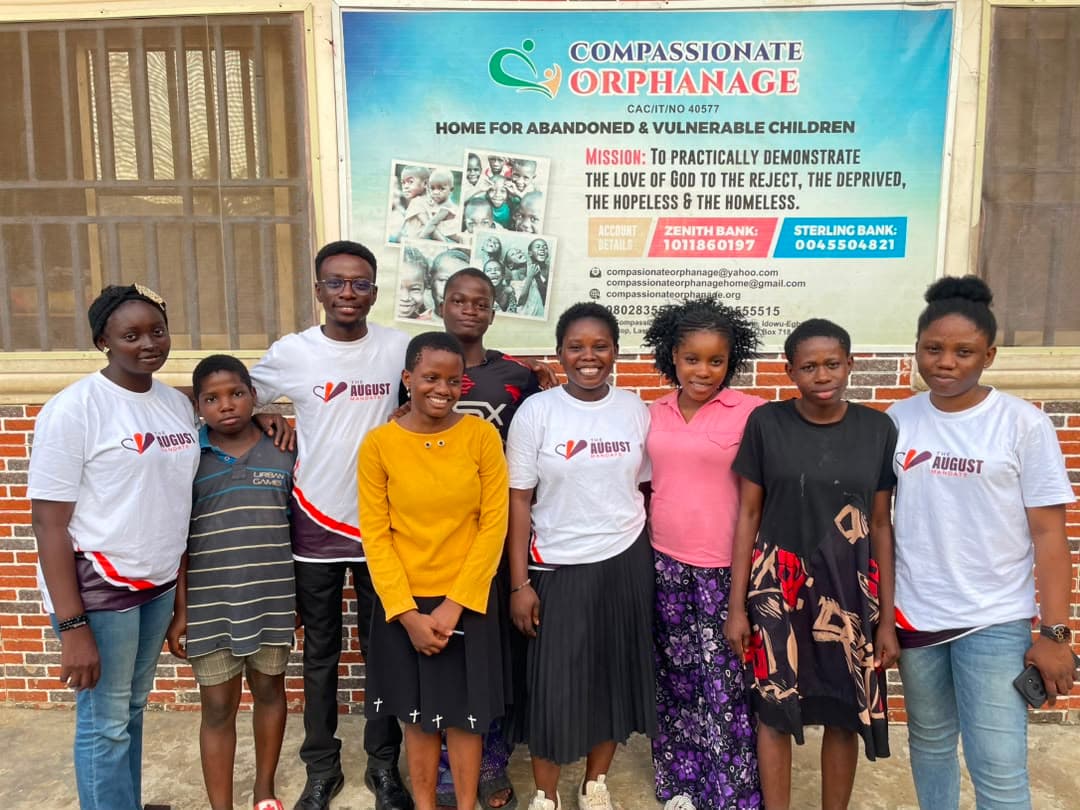 The August Mandate team standing with children in front of the orphanage banner